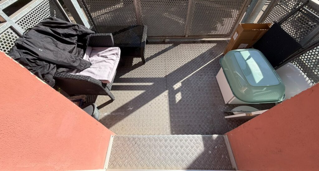Blick von der Balkontür auf meinen hinteren Balkon vor dem Umbau: Boden aus Riffelblech, Rattansessel und abgestellte Kisten