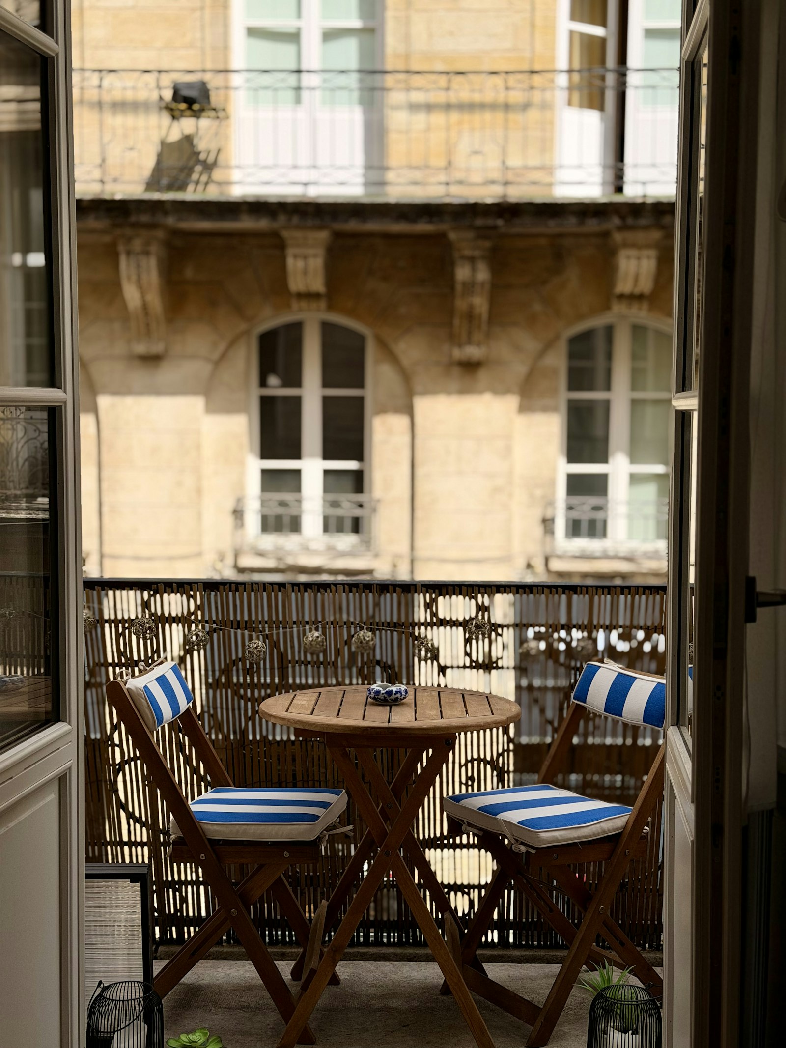Kleiner Balkon mit rundem Tisch und zwei Stühlen mit blau gestreiften Kissen