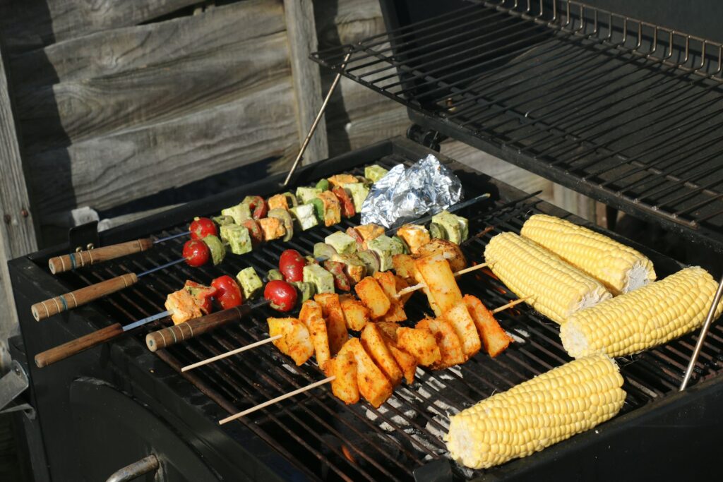 Grill mit Fleischspießen, Gemüsespießen und Maiskolben auf dem Rost