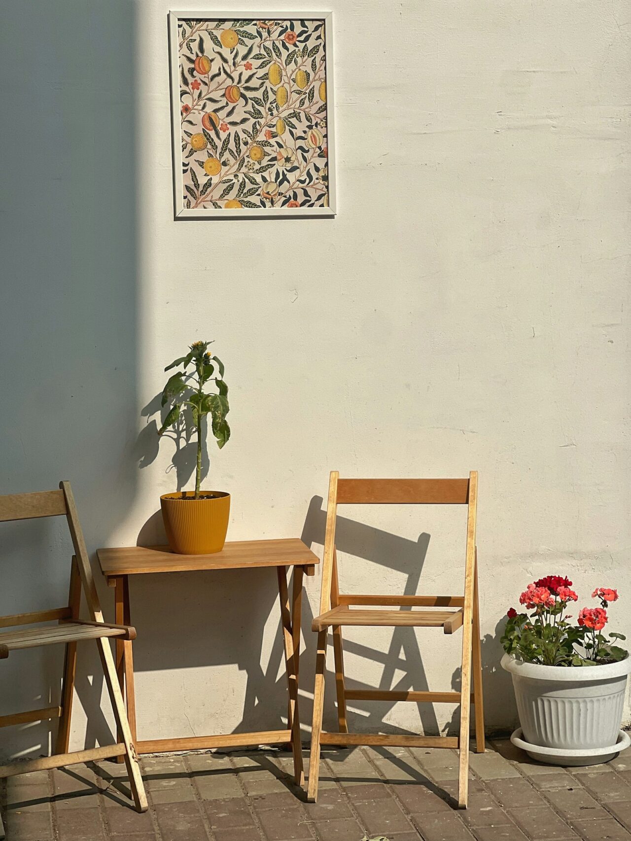 Zwei Klappstühle aus Holz und ein kleiner Tisch vor einer sonnigen Wand